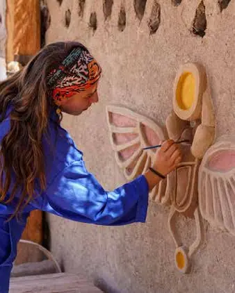 Artist sculpting a winged scarab on a mud wall